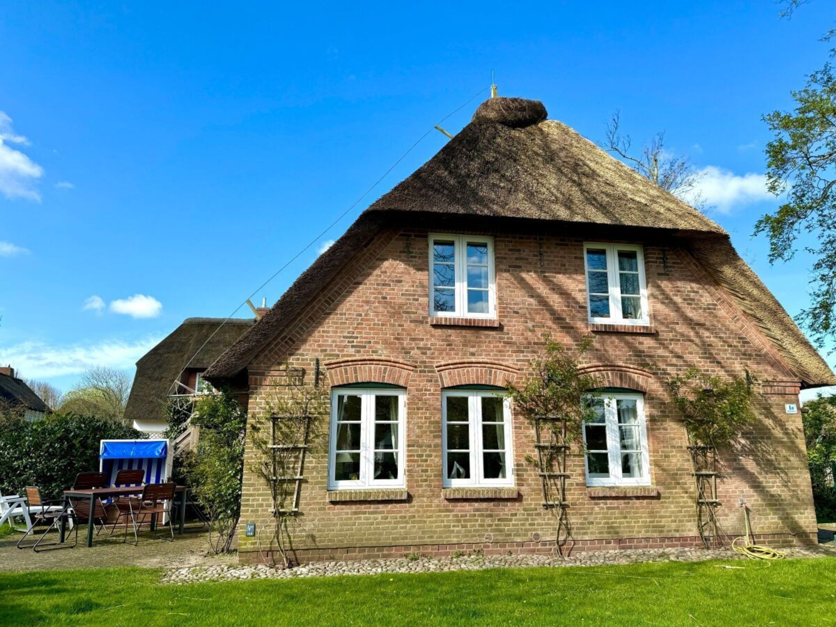 A brick house with a thatched roof, multiple windows, and a small garden area with a table and chairs.