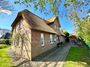 A brick house with a thatched roof, a paved driveway, and a bicycle parked outside. - Osterhus Nieblum (Nieblum)