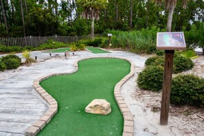 Een minigolfbaan met een kronkelend pad, groen kunstgras en een houten paal met een bordje.