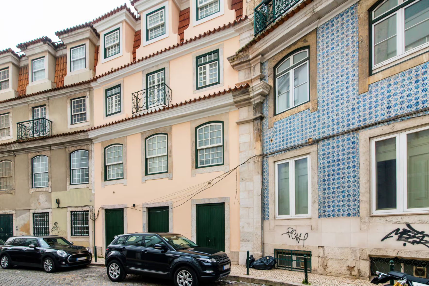 A row of buildings with multiple balconies and windows, a parked car, and a motorcycle.