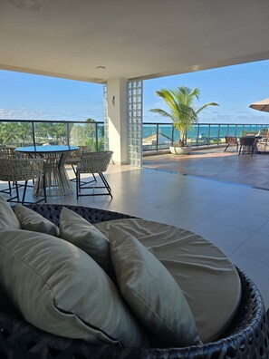 A spacious outdoor seating area with a view of the ocean, featuring a round table and wicker chairs. - MB I - Ap. 405 - Nico Uruguay (Ipojuca)