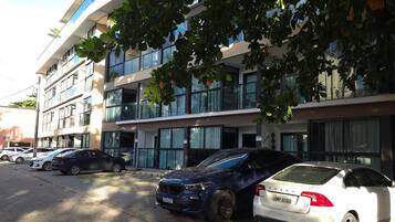 Un área de estacionamiento con varios automóviles, incluyendo un Volvo blanco y un SUV azul, frente a un edificio moderno con varios pisos y grandes ventanales.
