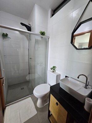A bathroom with a glass shower enclosure, a toilet, a sink, and a mirror. - MB I - Ap. 405 - Nico Uruguay (Ipojuca)