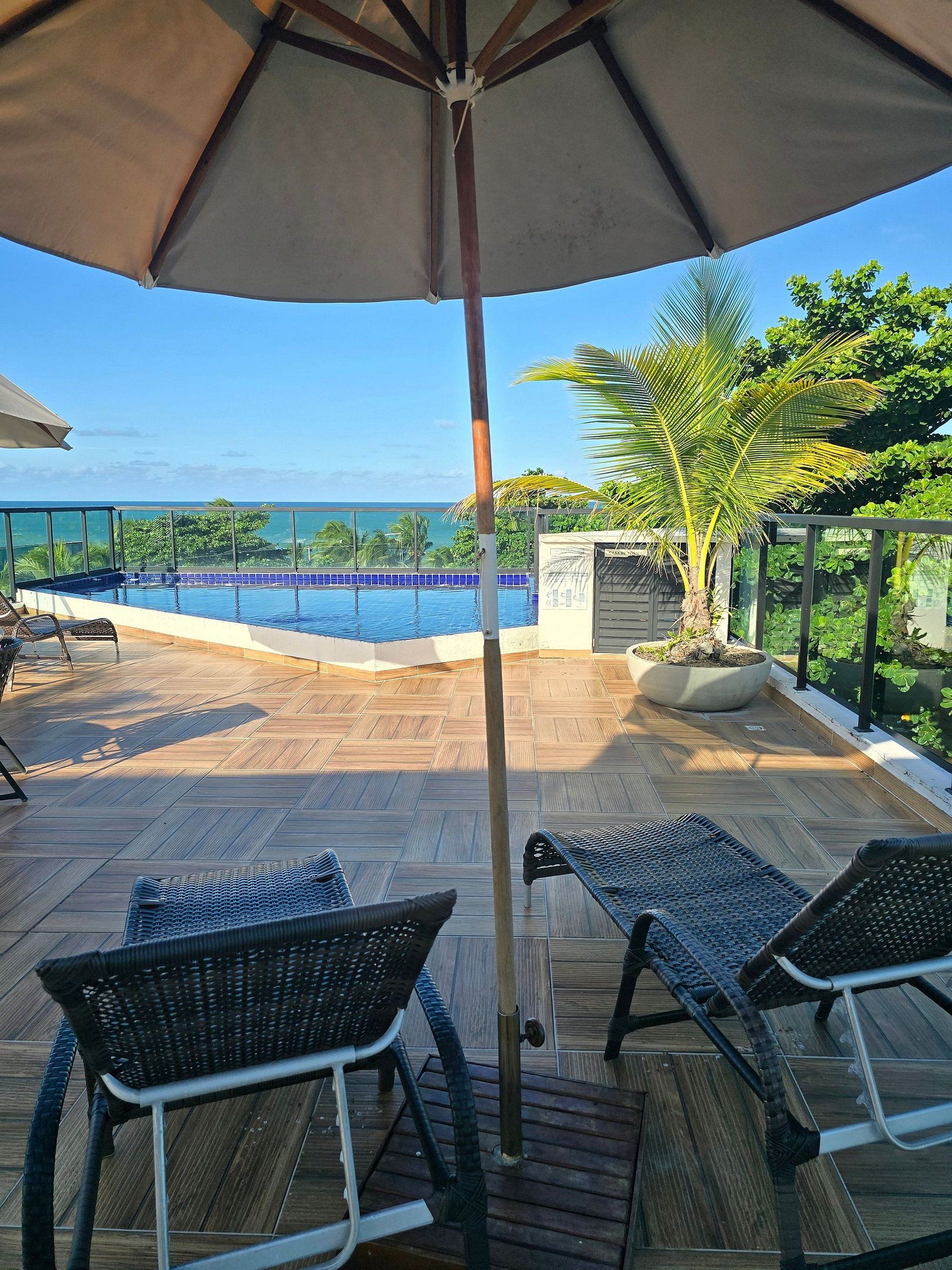Zona de piscina con vista al océano, muelle de madera y sillas de descanso.