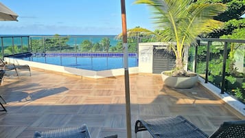 Zona de piscina con vista al océano, muelle de madera y sillas de descanso.