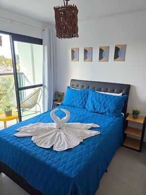 A bedroom with a large bed, a window with a view of palm trees, a wicker chandelier, and three wall art pieces. - MB I - Ap. 405 - Nico Uruguay (Ipojuca)
