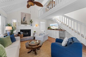 A spacious living room with a fireplace, a high ceiling with a fan, a staircase, and a view of the outdoors. - Seabrook Exclusives | 912 Sealoft (Seabrook Island)