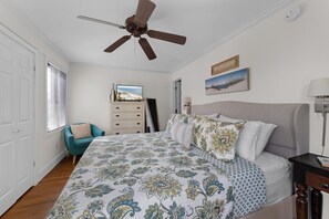 Een slaapkamer met een bed, een plafondventilator, een dressoir, een stoel en een televisie.