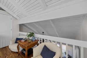 Een kamer met een schuine kap, een houten tafel met boeken en een vaas, twee stoelen en een raam met jaloezieën.