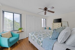 A bedroom with a bed, a ceiling fan, a television, a dresser, and a window with blinds. - Seabrook Exclusives | 912 Sealoft (Seabrook Island)