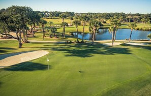 A golf course with a water body, palm trees, and a clear sky. - Seabrook Exclusives | 912 Sealoft (Seabrook Island)