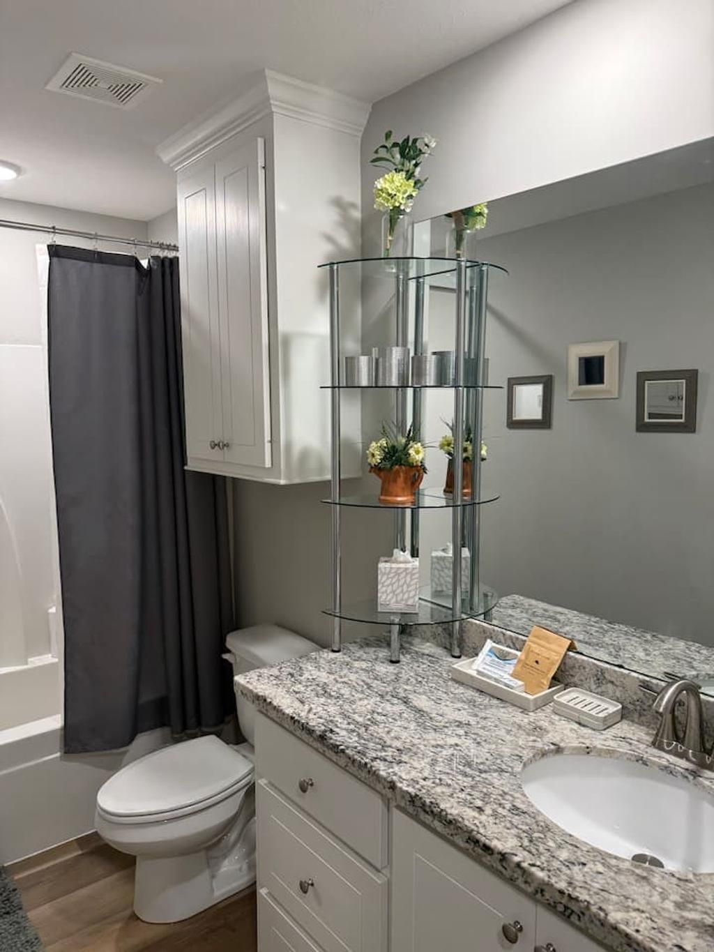 A bathroom with a white toilet, a glass shelf with toiletries, and a marble countertop.