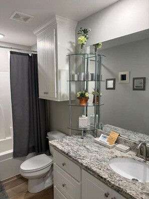 A bathroom with a white toilet, a glass shelf with toiletries, and a marble countertop. - Silver Hill (Pearl)
