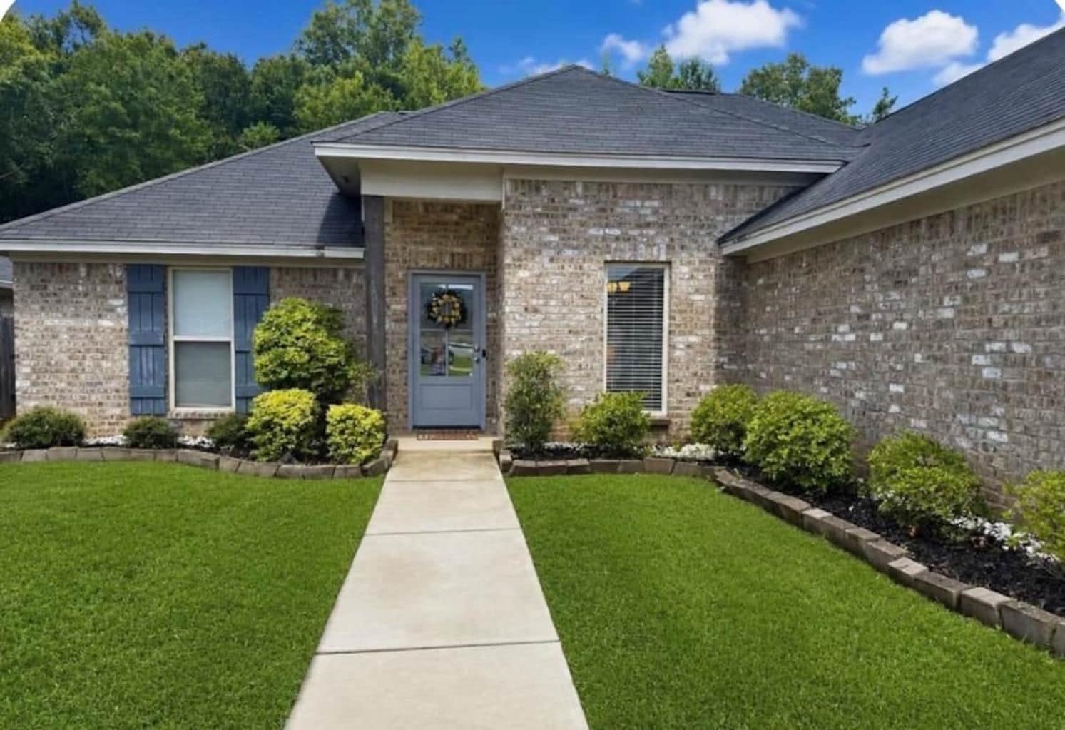 A two-story house with a stone facade, a front door with a wreath, and a well-maintained lawn.