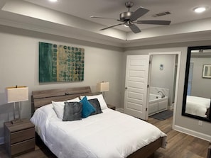 A bedroom with a bed, nightstands, a ceiling fan, a door, and a bathroom with a mirror. - Silver Hill (Pearl)
