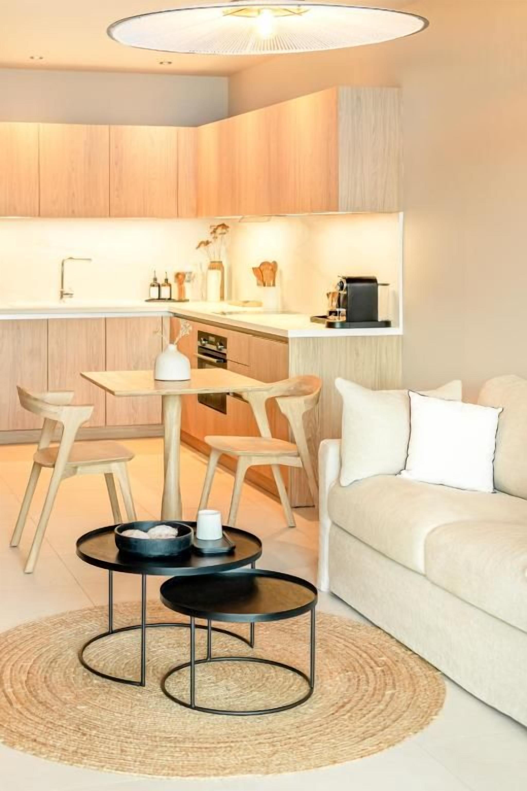 Una cocina moderna con armarios de madera, un comedor con mesa y sillas redondas, y una sala de estar con sofá y mesa de centro.