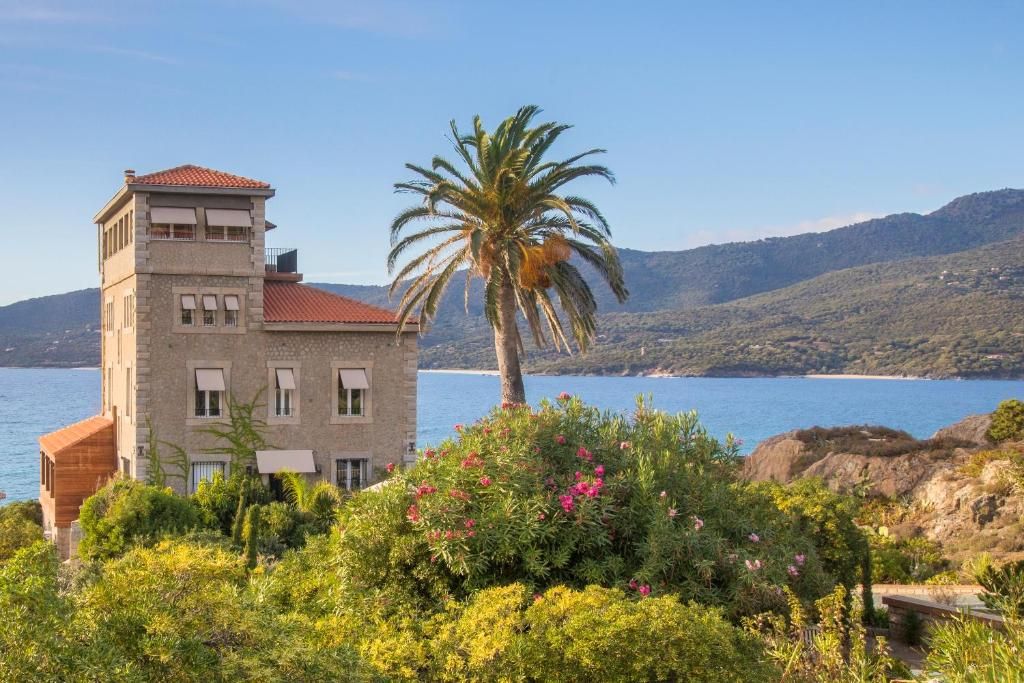 Un edificio costero con una torre, rodeado de exuberante vegetación y vistas al mar y colinas.