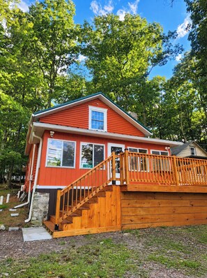 A red cabin with a wooden deck and a staircase leading to the entrance. - 3-BR Chalet in Lake Harmony - Lakeview, 6 Queen Beds, Fireplace, Walk to Town (Lake Harmony)
