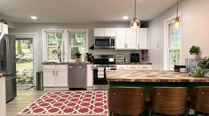 A modern kitchen with white cabinets, a stainless steel refrigerator, a microwave, and a stove. There are two windows with a view of the outdoors, a patterned rug, and a bar area with chairs. - 3-BR Chalet in Lake Harmony - Lakeview, 6 Queen Beds, Fireplace, Walk to Town (Lake Harmony)