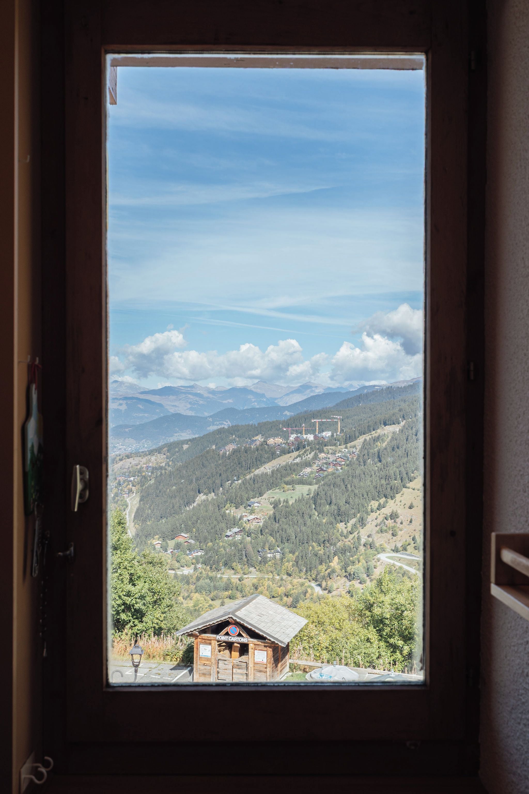 A window view of a mountainous landscape with a wooden cabin and a sign indicating a parking area.