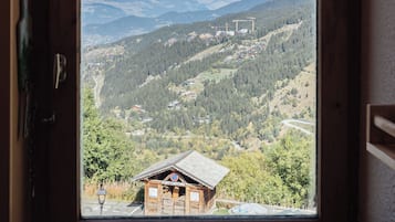 A window view of a mountainous landscape with a wooden cabin and a sign indicating a parking area.