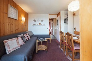 A cozy living room with a sofa, a small table, and a dining area with chairs. - Creux de l'Ours (Les Allues)