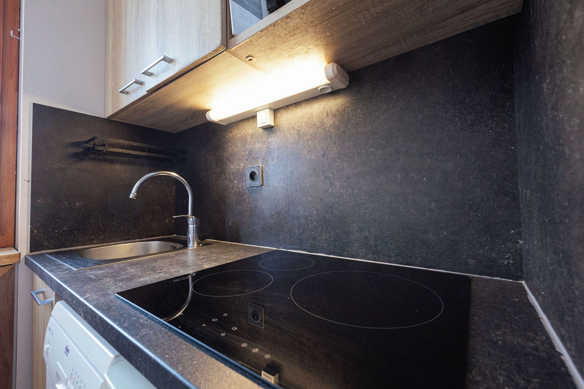 A kitchen with a black countertop, stainless steel sink, and a built-in electric stove.