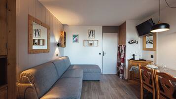 A cozy living area with a sofa, wooden cabinets, a dining table with chairs, and a television mounted on the wall.