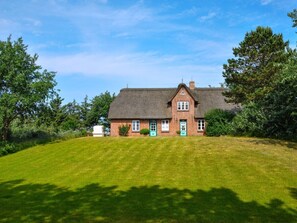 A traditional brick house with a thatched roof, surrounded by a well-maintained lawn and trees. - Karoline House Apartment Lise (Utersum)
