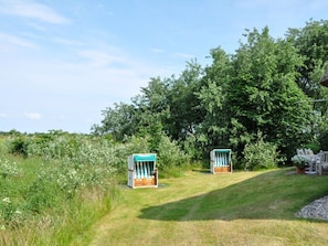 A grassy outdoor area with two wooden structures, possibly seating areas, surrounded by dense green foliage. - Karoline House Apartment Lise (Utersum)