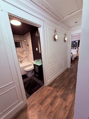 Un couloir avec des toilettes sur la gauche, comprenant des WC, un lavabo et un mur en marbre.