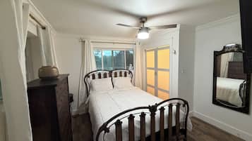 A bedroom with a bed, a dresser, a ceiling fan, a window with curtains, and a mirror on the wall.