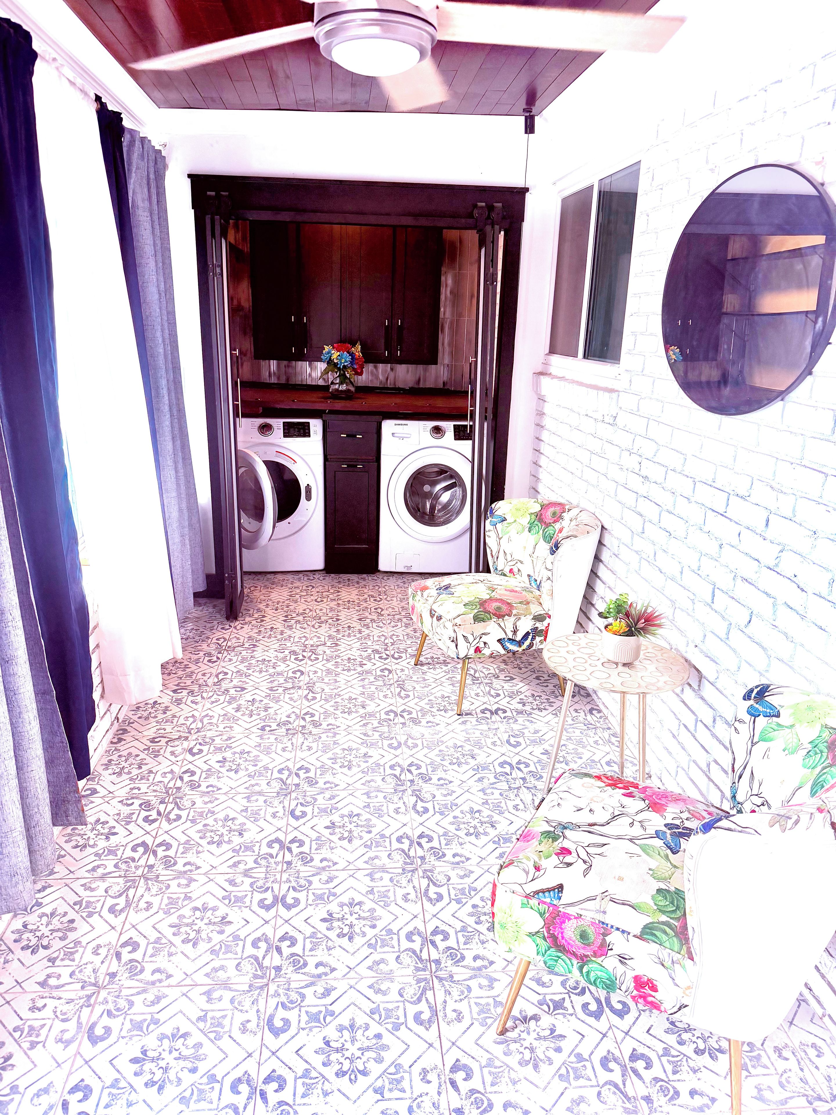 A laundry area with a washing machine and dryer, a patterned floor, and a chair with floral upholstery.