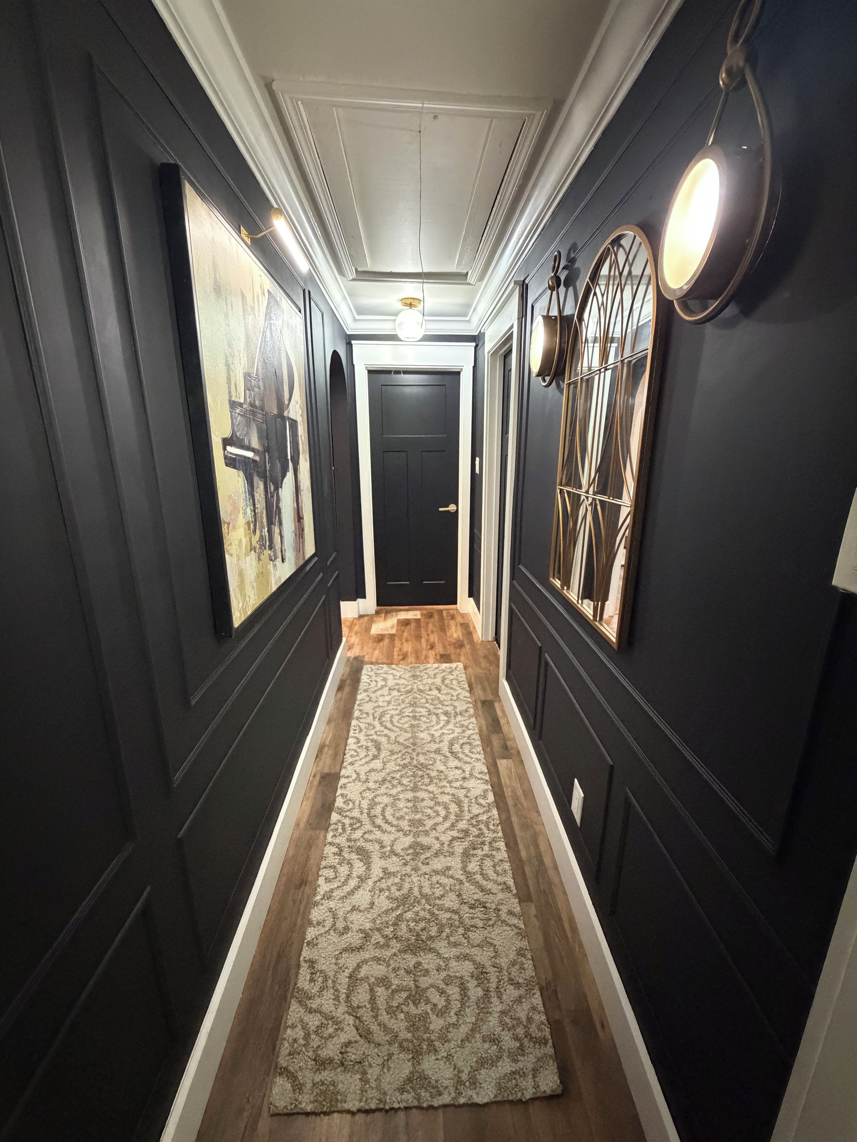 A hallway with dark walls, a patterned rug, and a door at the end.