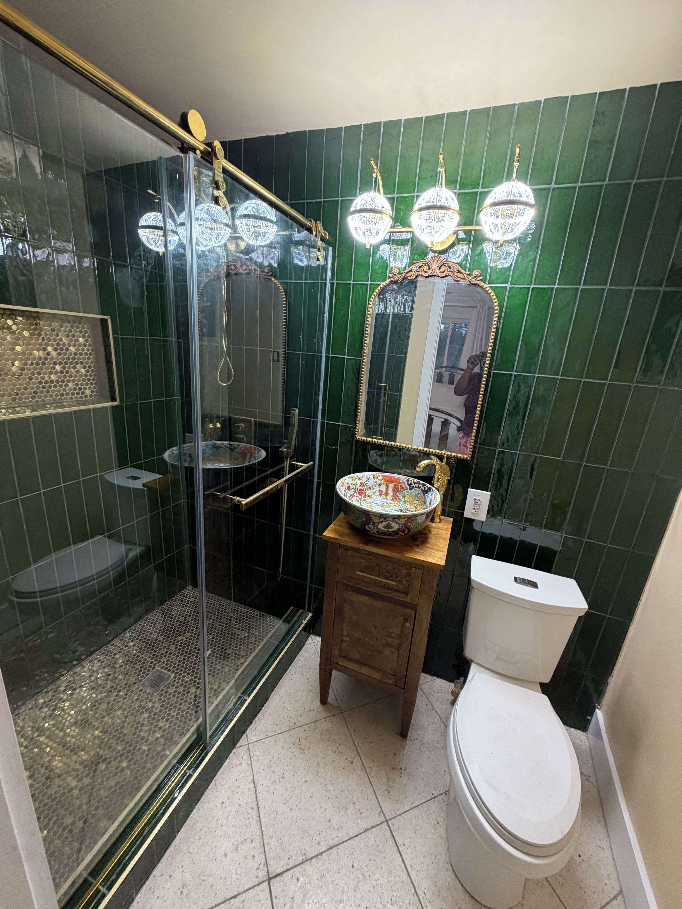 Kylpyhuoneessa on lasiseinällä varustettu suihku, wc ja pesuallas, jonka päällä on koristeellinen malja.