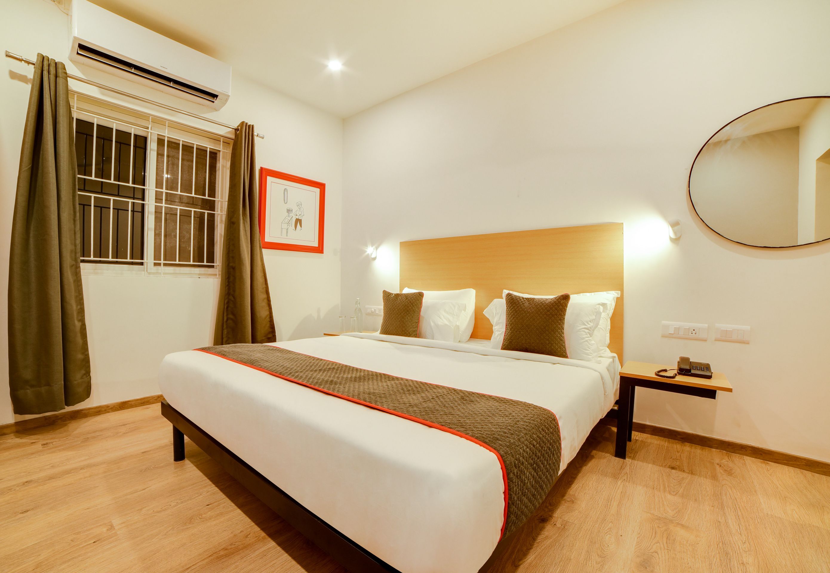 Habitación de hotel con una cama grande, una mesita de noche con teléfono, una ventana con cortinas y un espejo instalado en la pared.