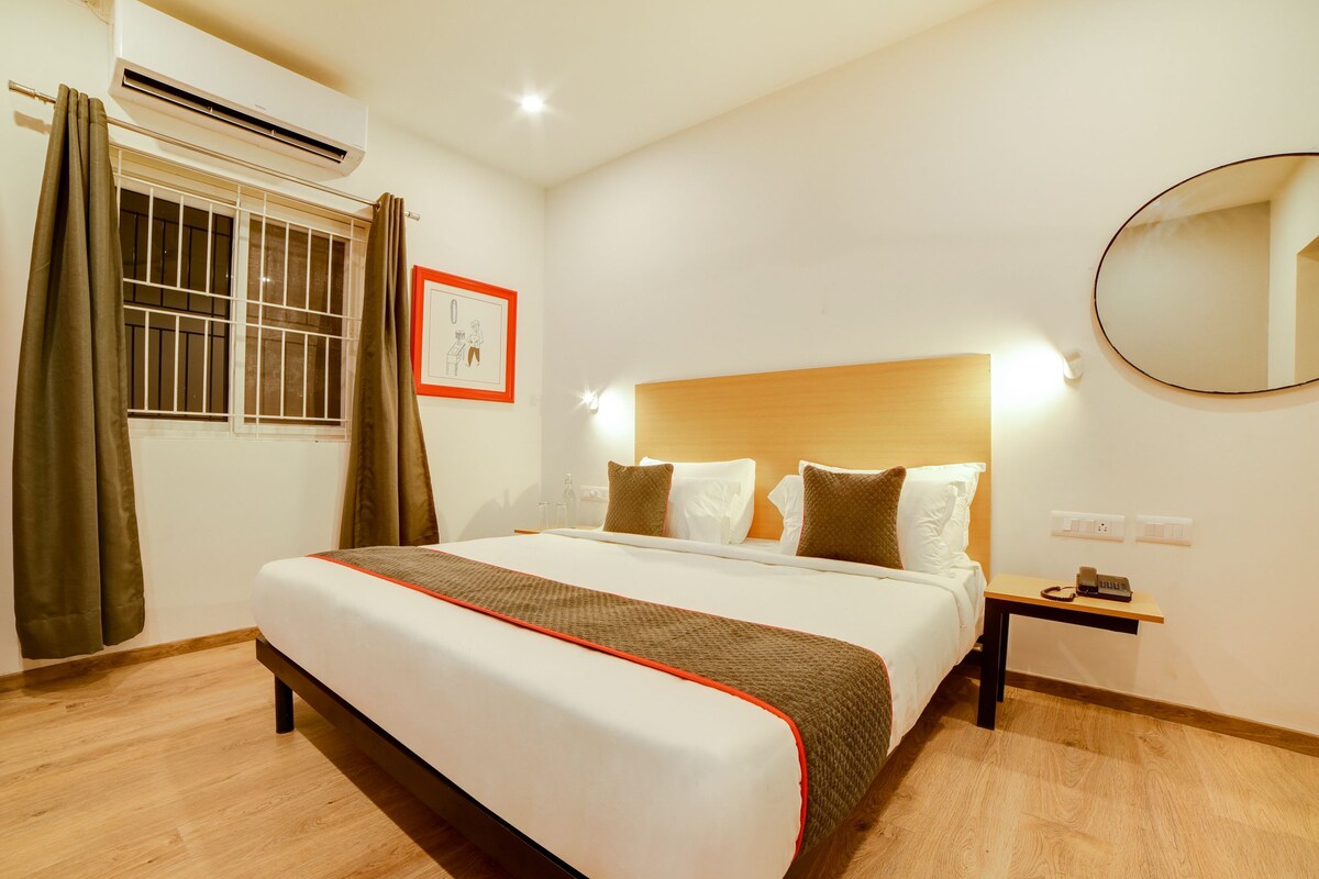 Habitación de hotel con una cama grande, una mesita de noche con teléfono, una ventana con cortinas y un espejo instalado en la pared.