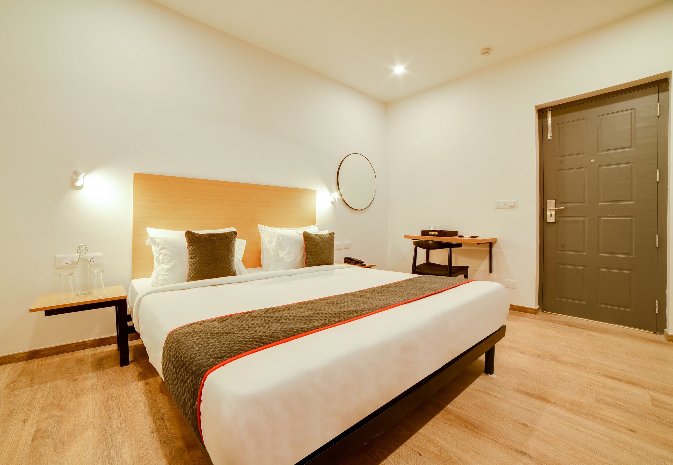 Habitación de hotel con una cama grande, una mesita de noche, un espejo, una puerta y una pequeña mesa con una silla.