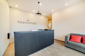 Una recepción con diseño moderno, un sofá gris con cojines rojos, y un letrero en la pared que dice 'TOWNHOUSE'.