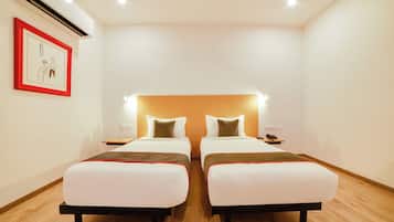 Una habitación de hotel con dos camas, una mesita de noche, un cuadro enmarcado y un equipo de aire acondicionado.