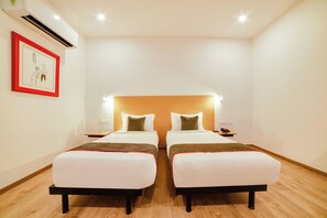 Una habitación de hotel con dos camas, una mesita de noche, un cuadro enmarcado y un equipo de aire acondicionado.