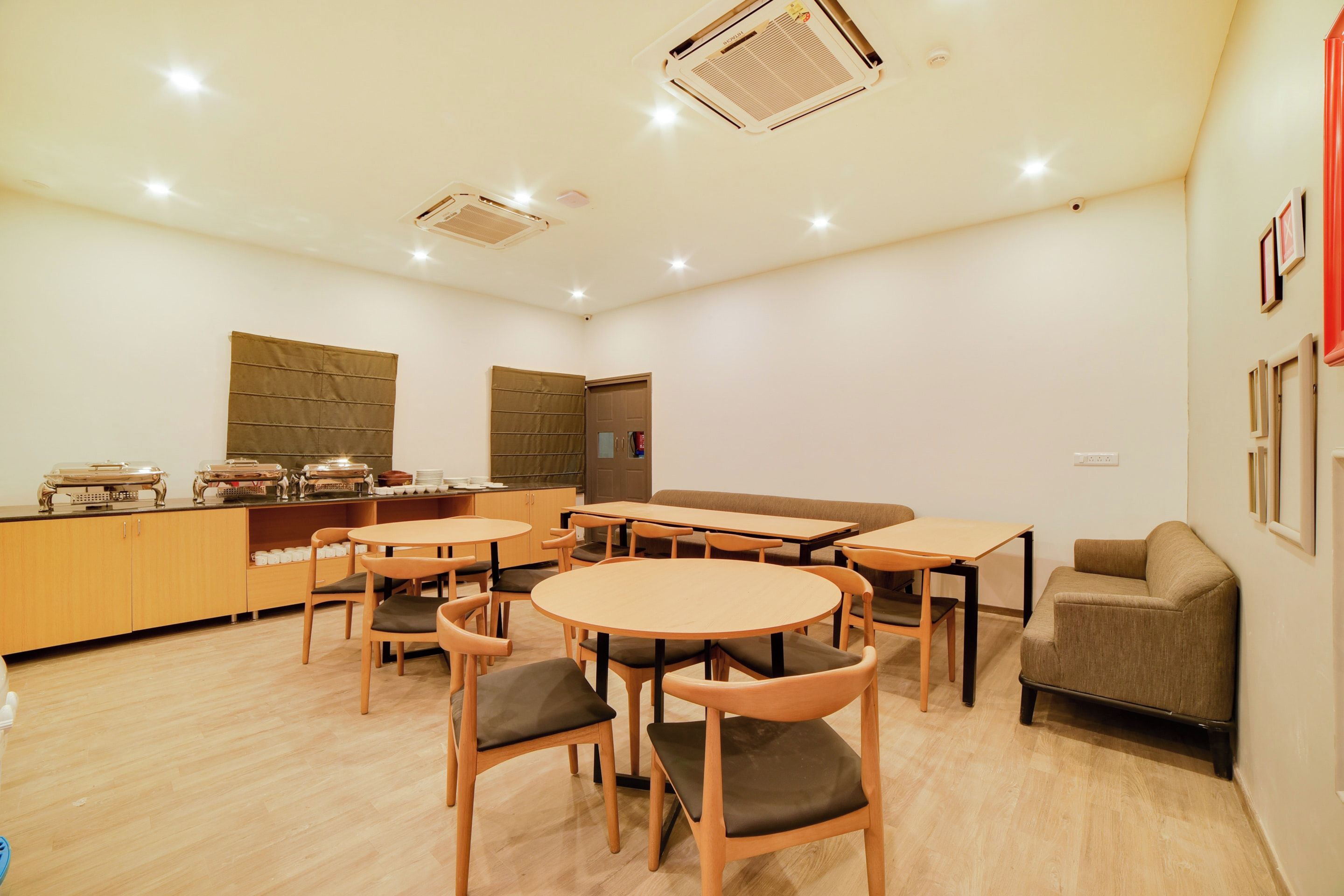 Un comedor moderno con mesas y sillas de madera, una barra con equipo para servicio de alimentos y un sofá.