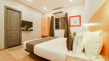 A hotel room with a bed, a television, an air conditioning unit, a window with curtains, and a framed picture on the wall.