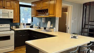 A kitchen with wooden cabinets, a built-in microwave, a granite countertop island with bar stools, and a view through the window.