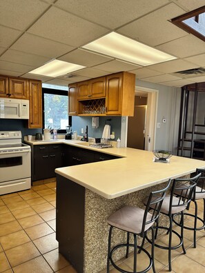 A kitchen with wooden cabinets, a built-in microwave, a granite countertop island with bar stools, and a view through the window.