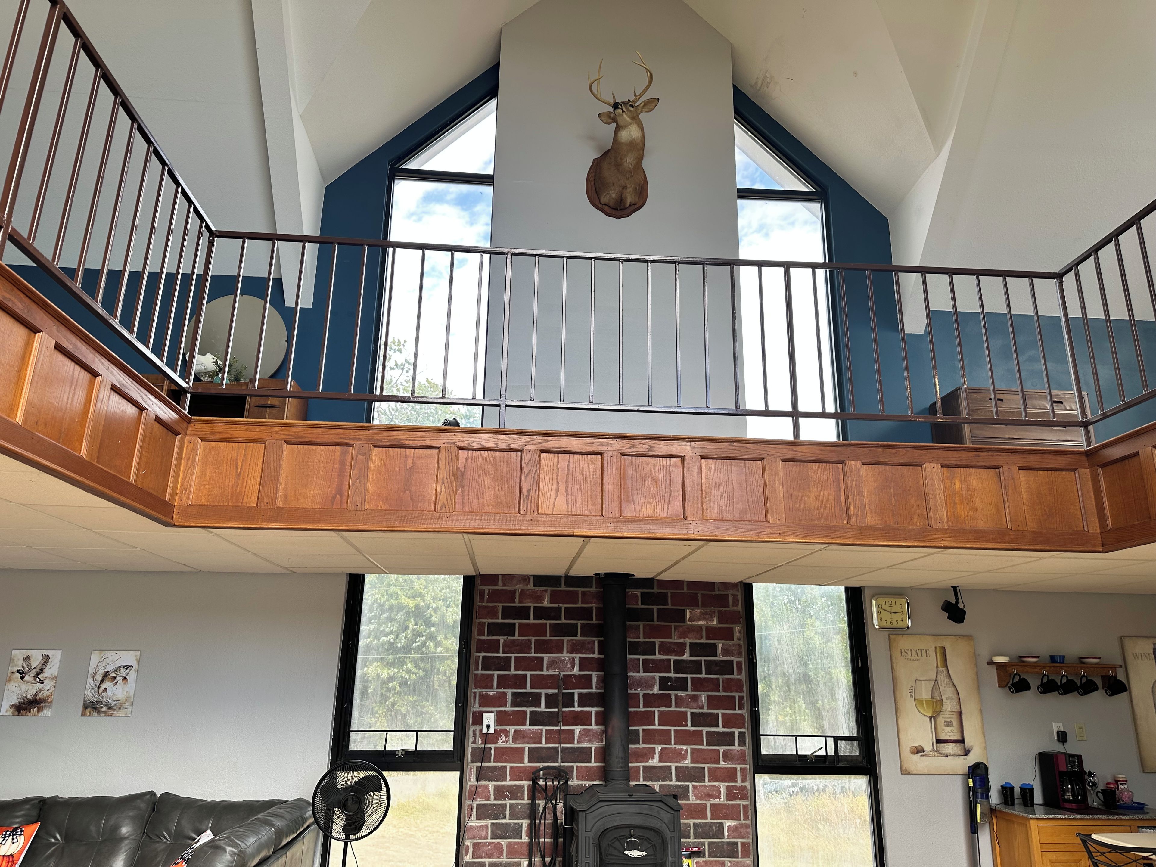 A loft-style room with a wooden balcony, a stone fireplace, and a mounted deer head.