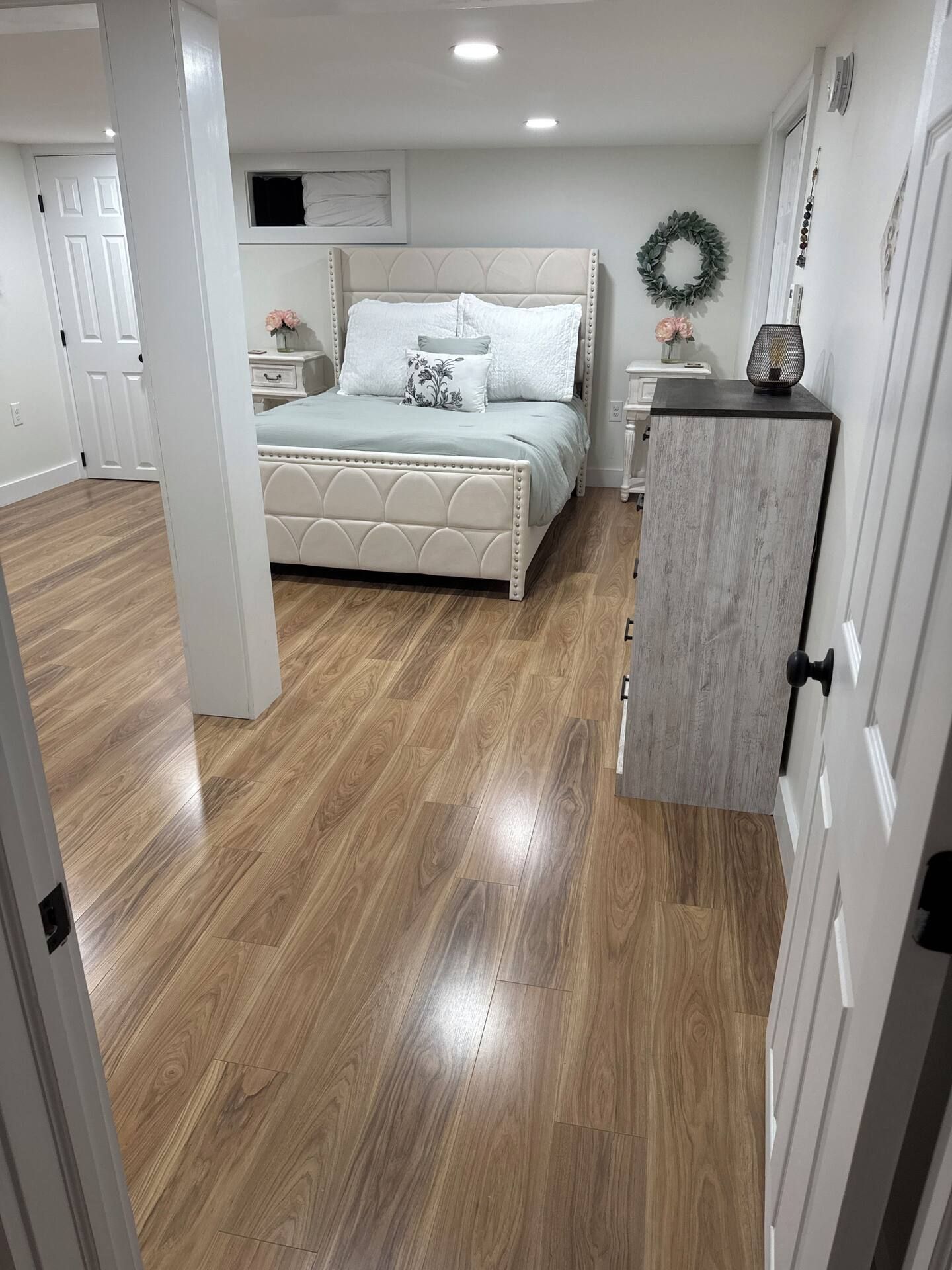 A bedroom with a bed, a nightstand, a dresser, and a wall-mounted wreath.