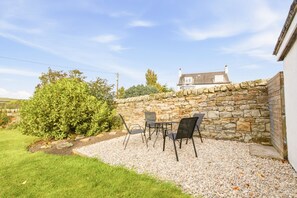 Eine Terrasse mit einer Steinsäule, einem kleinen Tisch und Stühlen sowie einer Hecke.