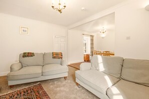 A living room with two sofas, a patterned rug, and a dining area with a table and chairs. - Hillside Cottage - North East Escapes (East Ord)