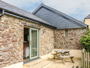 A stone building with a green door, a wooden bench, and a small table with a bottle. - Beech Cottage (Truro)